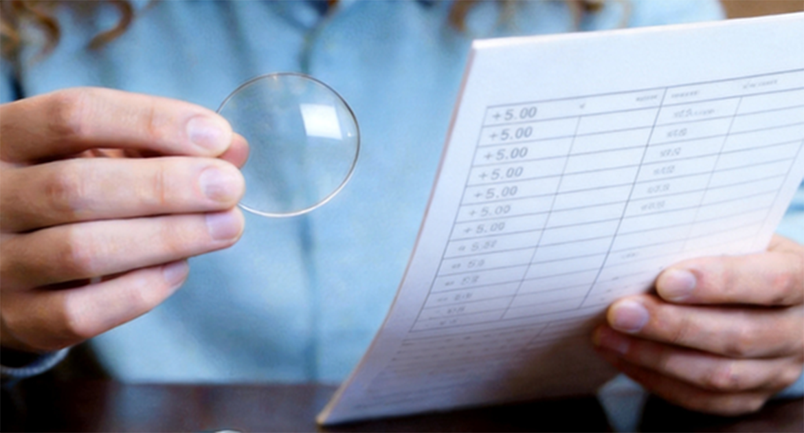 A person holding a lens over a paper eyeglass prescription to check the match